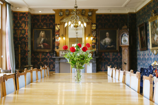 A dining table for large dinner parties in a traditional Dutch interior with a vase of red roses.