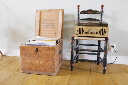 A collection of records in a wooden box and a vintage turntable on a antique chair.