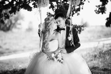 Black and white. Wedding. Wedding day. Married, cute couple near the swing after wedding ceremony. Beautiful bride with bouquet of flowers and elegant groom walking after wedding ceremony.