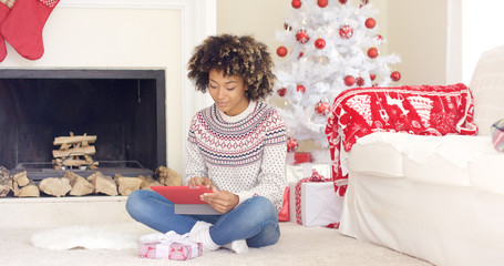 Young woman surfing the internet at Christmas sitting on the floor in the living room with a tablet pc in front of the tree