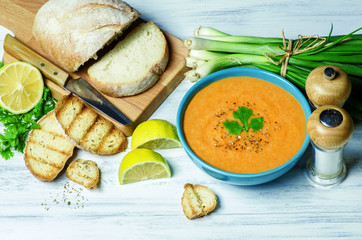 Delicious lentil soup in blue bowl placed with fresh ciabatta bread,lemon, green onion and toasted bread on white wooden background.Top view..Copy space.