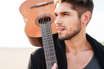 Man walking at the beach and holding guitar on shoulder