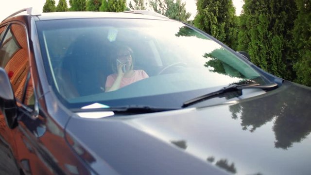 Pretty girl in a skirt sitting in car, smiling and using phone