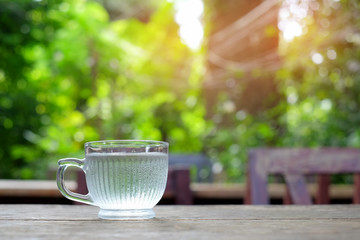 Glass water on wooden table with green blurred background.