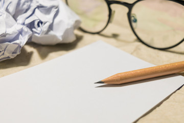 Blank paper and pencil on the table with crumpled paper and glasses beside
