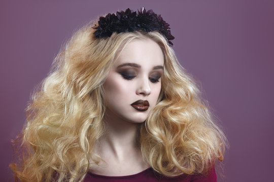 Beauty portrait of a beautiful young blonde woman with gothic make-up and decorative wreath on a purple background.