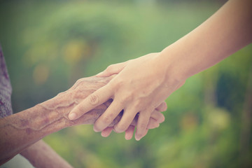 Old and young holding hands on light background, vintage tone.