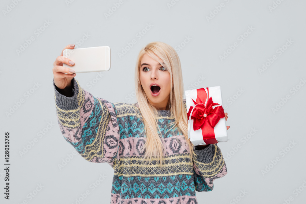 Canvas Prints Excited young blonde woman holding gift box and taking selfie