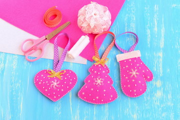 Christmas tree decorations. Handmade pink felt Christmas tree, heart, mitten decorations, sewing supplies on blue wooden background with copy space for text. Winter crafts project. Closeup. Top view