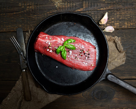 raw veal meat in a frying pan on a wooden background.Top view.