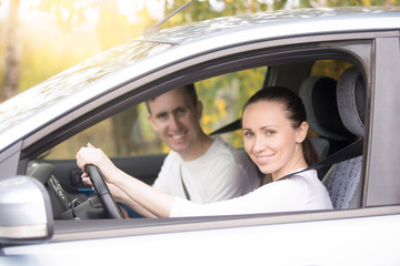 Lifestyle portrait of young confident happy woman driving, smiling casual man sitting near in the car, family travelling by car, woman taking driving courses