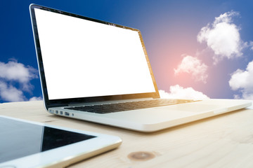 Office table with blank screen on laptop and cloudy sky backgrou