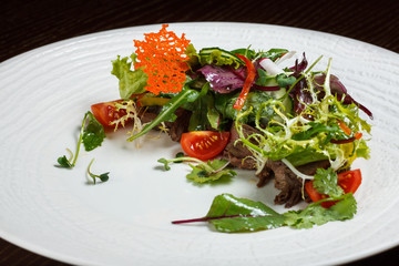 Vegetable salad menu for the restaurant in a large white plate on a white table cloth on a wooden table. Salad on the table with knife and fork. Svezhive vegetables.
