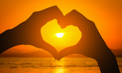Naklejka premium Silhouettes hand heart shaped with sunset and sea