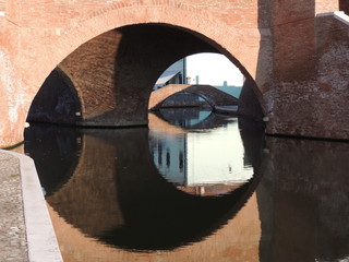 archi di mattoni dei ponti sopra i canali di Comacchio che si riflettono nell'acqua  - obrazy, fototapety, plakaty