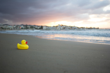 Yellow small toy duckling on sand beach in evening. Crete, Greece.