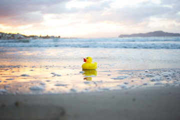 Yellow small toy duckling on sand beach in evening. Crete, Greece.