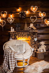 Bulbs garland lights and decorativa hearts at the wooden boards wall above firewood fireplace. Winter holiday background