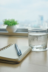 Notebook and coffee on wooden table at window, urban background with blurred buildings
