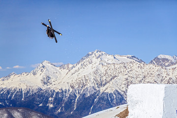 Fototapeta premium Skier flying from a ski jump making figure on blue sky and snowy mountain peaks background