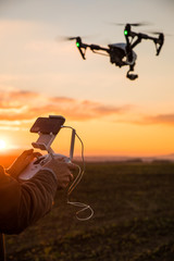 Man controls the fly of quadrocopter in field over sunset background - obrazy, fototapety, plakaty