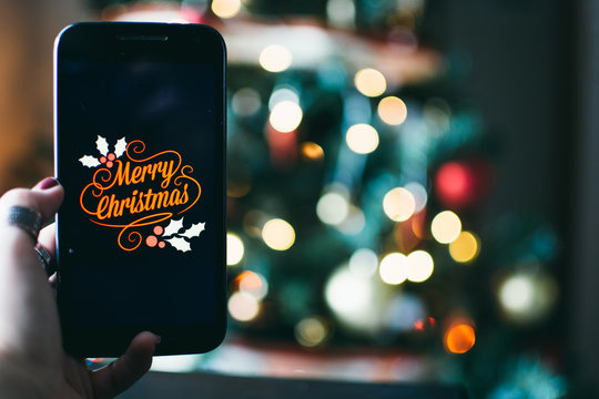 person takes a photo on a smartphone of merry christmas with a christmas background