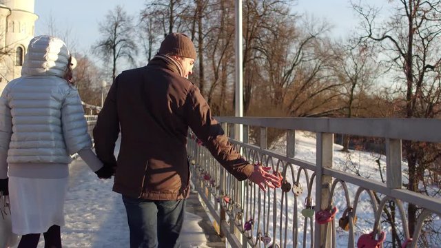 Man and woman walking holding hands on a small bridge full of love locks. 4K steadicam shot, back view