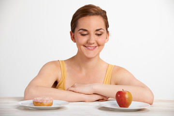 Young Woman Choosing Between Doughnut And Cake For Snack