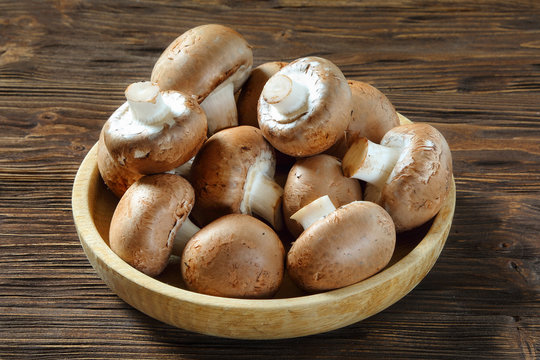 Portobello champignons in a wooden bowl on a brown table