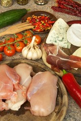 Raw chicken breast fillets on kitchen breadboard. Preparation of home diet meals with vegetables and cheese. Dietary chicken meat.
