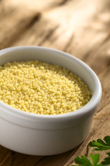 Raw couscous in small bowl on wood photographed with natural light (Selective Focus, Focus one third into the couscous)