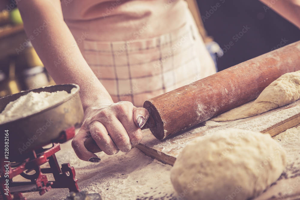 Wall mural Close up of female baker hands kneading dough and making bread with a rolling pin. Retro look.