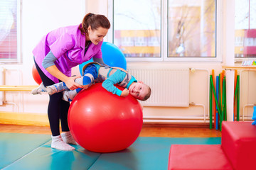 cute kid with disability has musculoskeletal therapy by doing exercises in body fixing belts on fit ball © Olesia Bilkei