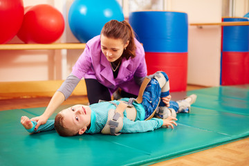 cute kid with disability has musculoskeletal therapy by doing exercises in body fixing belts