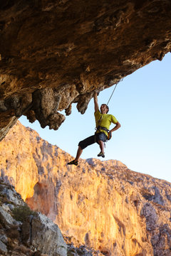 Male rock climber hanging with one hand on a cliff while putting chalk on another