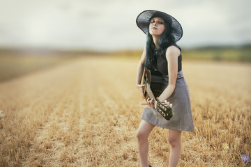 Mujer tocando la guitarra en un campo de verano al atardecer - obrazy, fototapety, plakaty