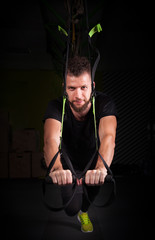 Fototapeta na wymiar one handsome young muscled man training with trx while working out in gym
