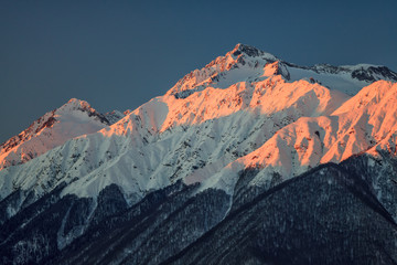 Beautiful mountain scenic winter landscape of the Main Caucasian ridge with snowy peaks on blue sky background at sunset