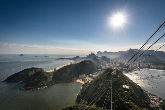View of Rio de Janeiro city from the Sugarloaf Mountain with sun in the sky and a cable car approaching