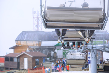 Skiers' legs on a cableway chair ski lift in cloudy snowy winter mountains close up
