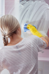 Young lady wiping mirror with blue cloth and special cleaning