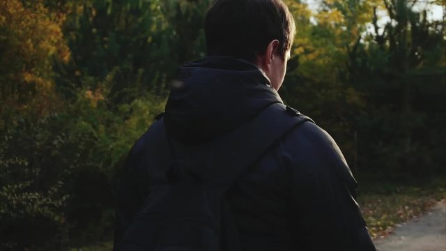 Young man in black jacket walking in the autumn park using his smartphone HD