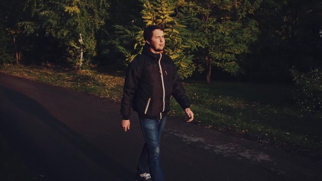 Young calm man in black jacket walking in the autumn park dramatic light slow motion HD