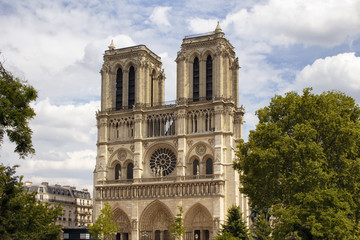 Fototapeta na wymiar View of Notre Dame Cathedral with trees and cloudy sky in Paris. Towering, 13th-century cathedral with flying buttresses & gargoyles, setting for Hugo's novel.