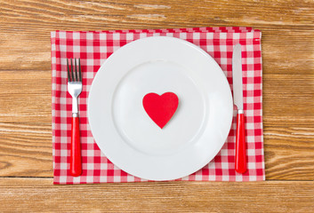 Red heart on a white plate.Tableware on wooden table.