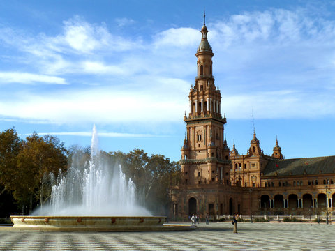 The fountain and the stunning tower of Plaza de Espana under cloudy blue sky, Seville, Spain 