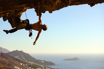 Young man climbing on roof of cave, view of coast below