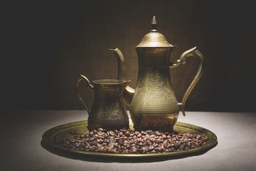 Vintage still life with heap of coffee beans near old copper coffeepots on bronze tray against...