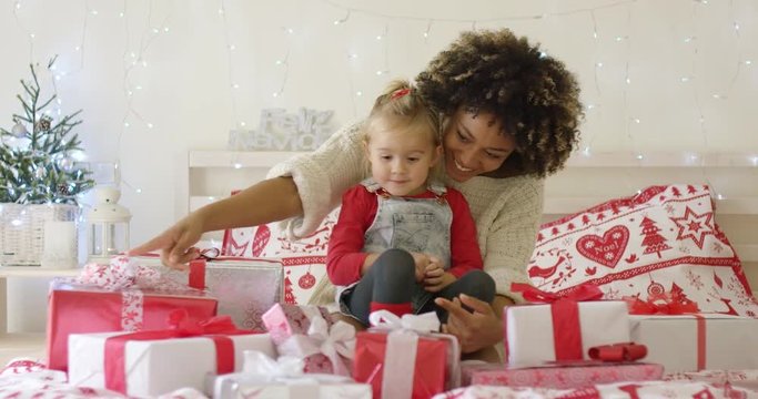 Cute excited daughter and mother in bed with various sized white and red wrapped Christmas gift boxes