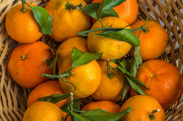 fresh orange tangerines with green  leaves in a basket